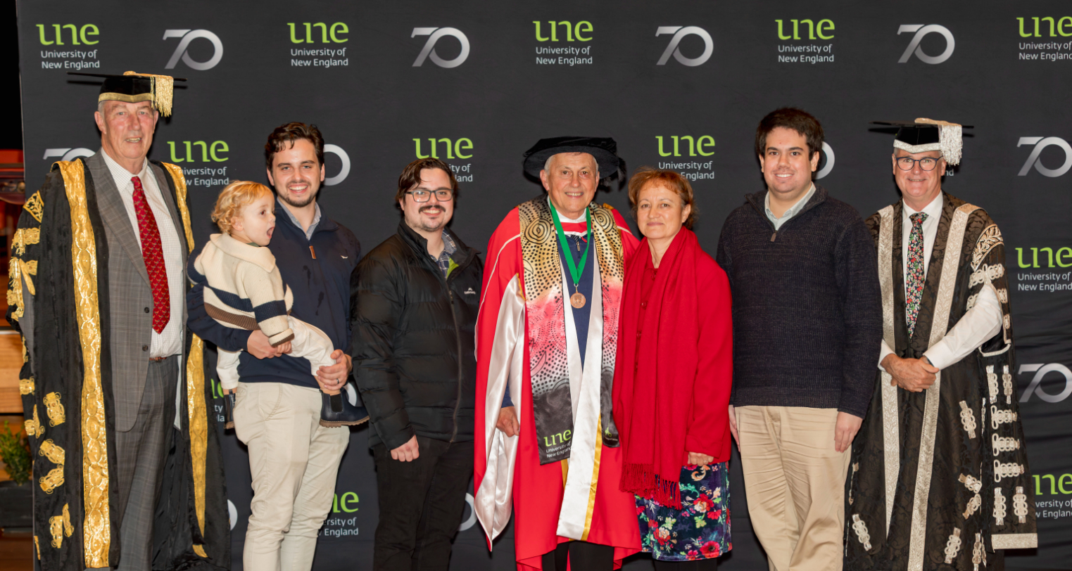 Male senior in graduation gown poses for formal photo with his family and university Chancellor and Vice Chanceelor