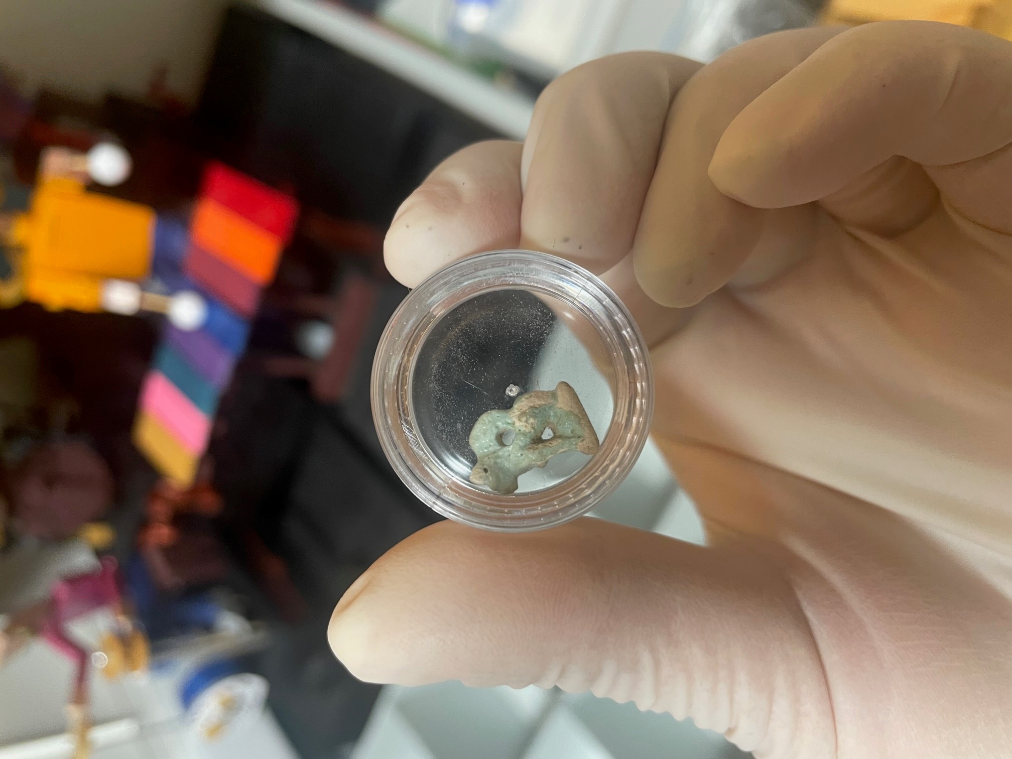 Hand inspects a small jade green amulet in a glass container 