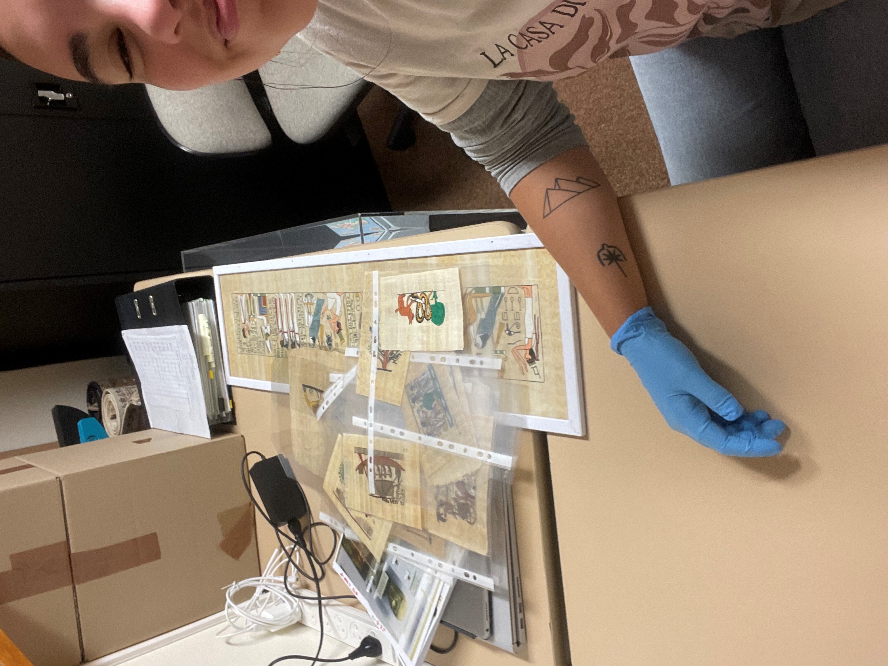 Casual selfie image of Dani Borrillo at a desk with sheets of heiroglyphics to decipher