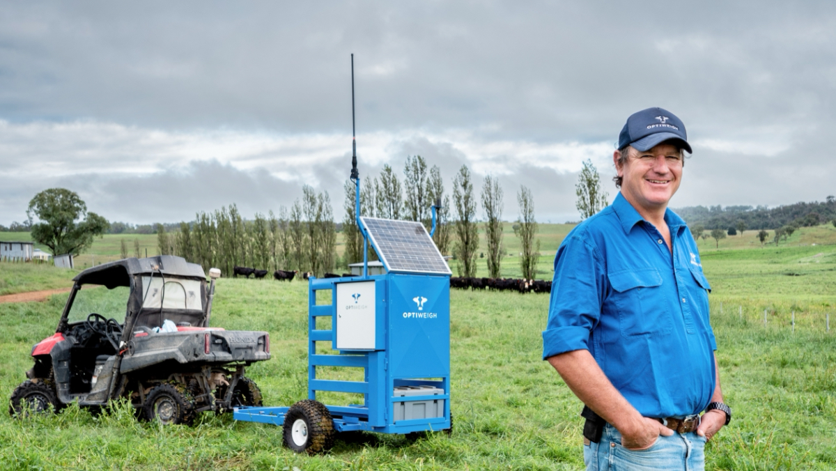 man standing in green paddock with machine in background