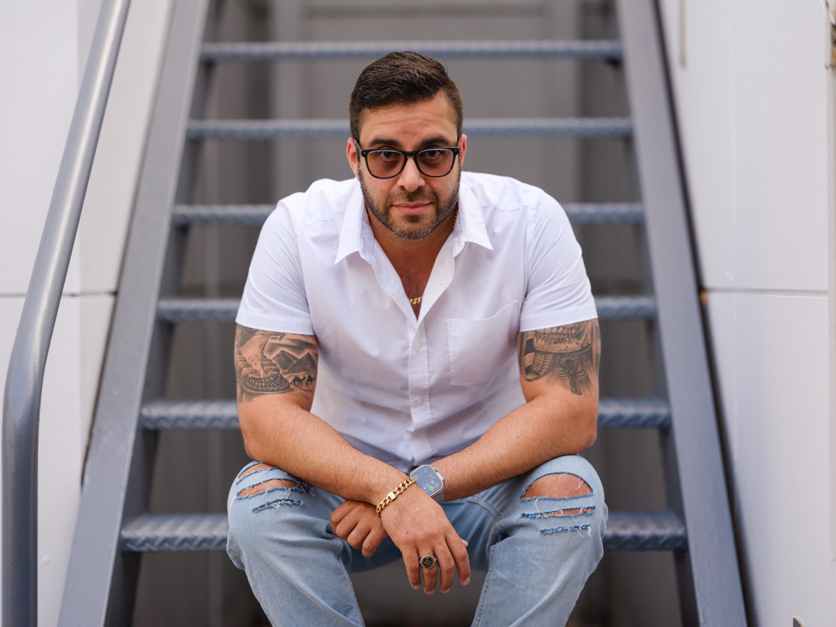 Man in sunglasses seated on steps, looking at camera.