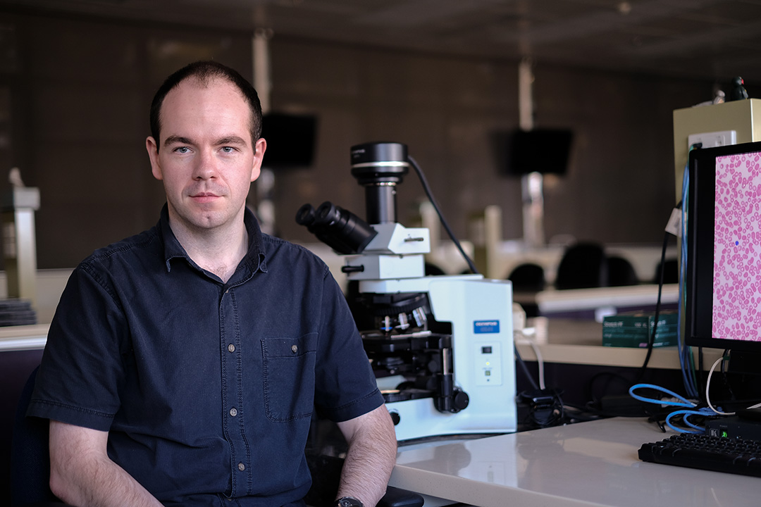 Dr Richard Charlesworth sitting in front of a microscope.