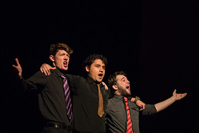 Three male students singing and raising their arms exuberantly