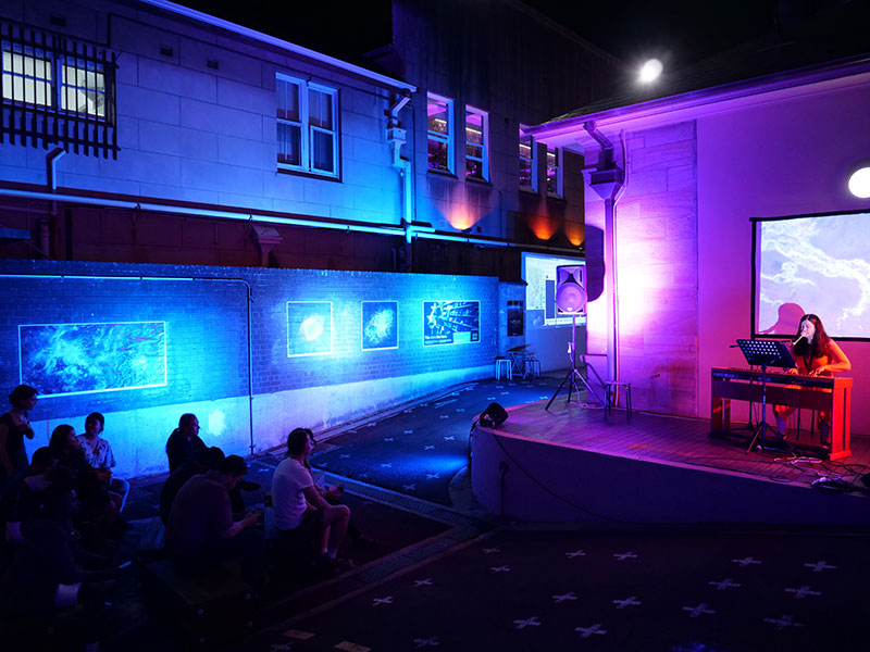 Colour-lit room with people in the audience and musicians on a stage.