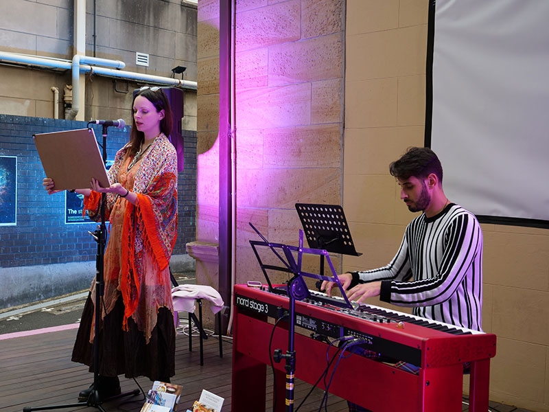 Valentina reciting poetry on stage with a keyboardist in the background