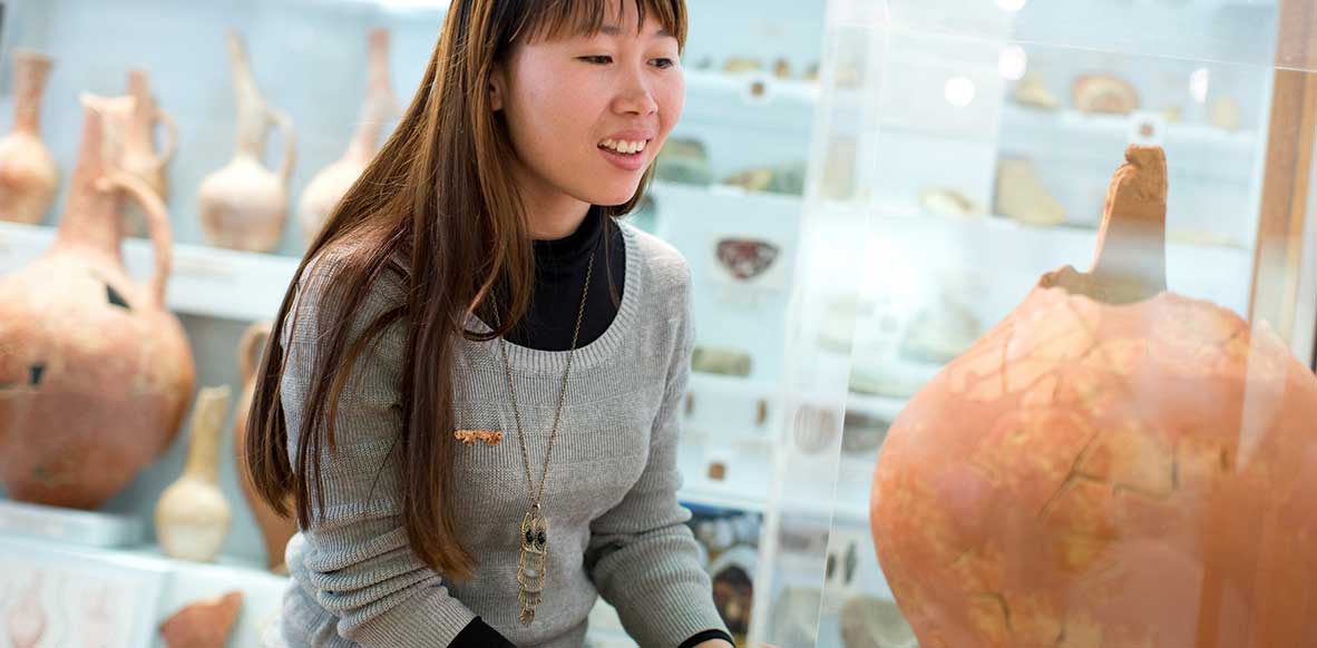 Female student looking at an ancient clay vessel in UNE's Museum of Antiquities.