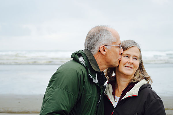  An older couple on a beach, the man kissing the woman on the cheek 