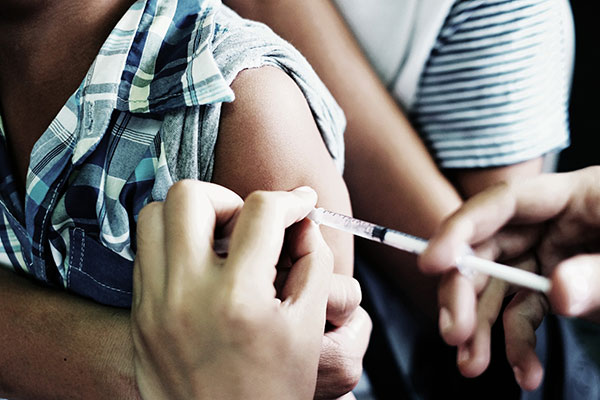 Closeup of a vaccination needle going into a young person's arm.